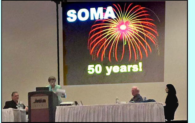 Photo shows people on a large stage with a podium and table, the slide behind them shows fireworks and says 'SOMA 50 years!'